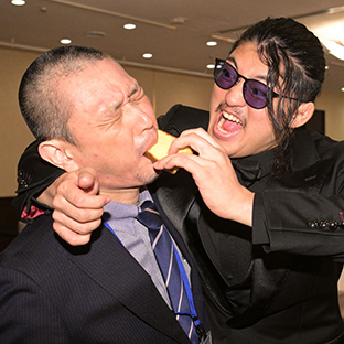 記者の口にカステラを押し込むOZAWA(右)